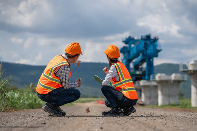 Survey team is working with a theodolite and road construction plans. Civil engineers are taking measurements with surveying tools during the construction.