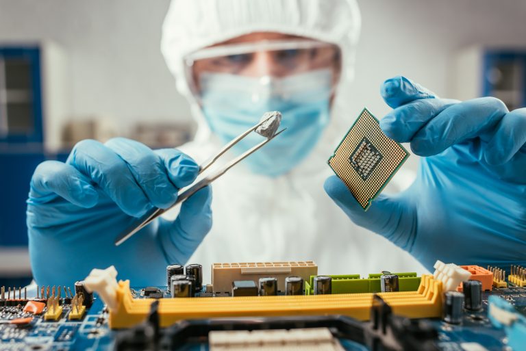 selective focus of engineer holding small stone with tweezers and microchip near computer